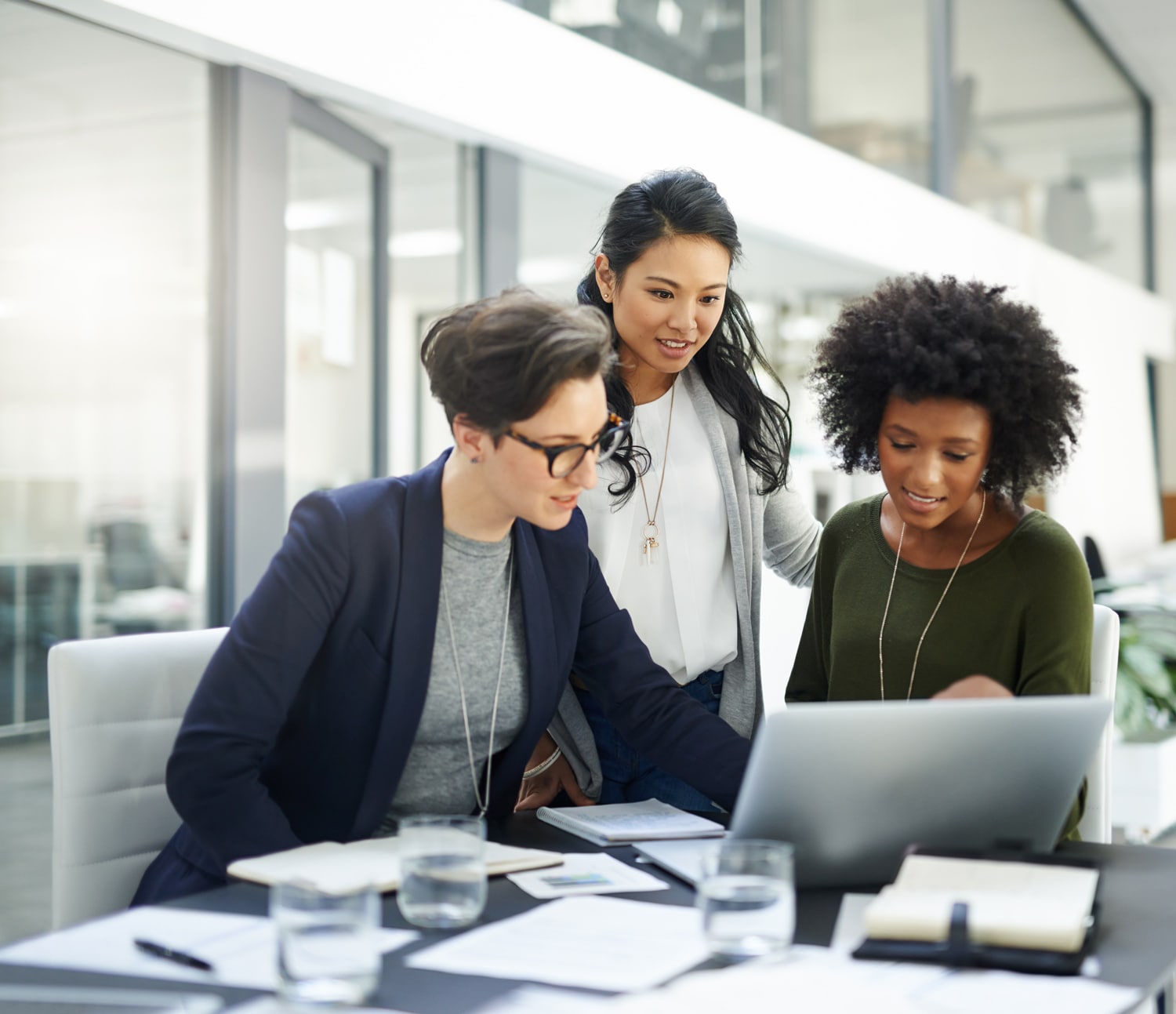 Three businesswomen gather around a laptop, comparing details. 