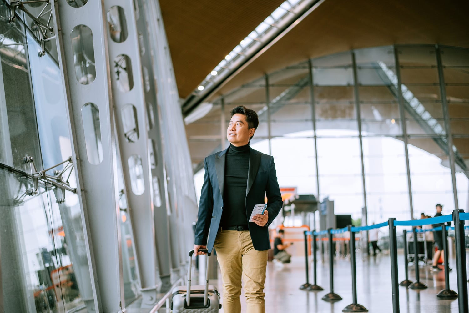 A businessman in a sleek turtleneck and blazer makes his way through the airport.