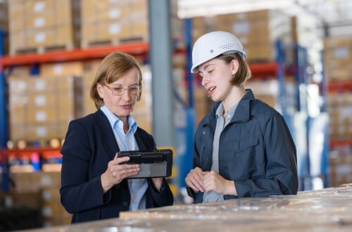 Two women on warehouse floor looking at tablet