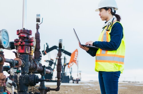 Woman in hard hat holding laptop in an oil field