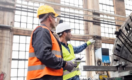 Two men in hard hats discussing factory machinery