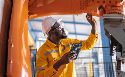 Man in hard hat holding smartphone and inspecting pipes