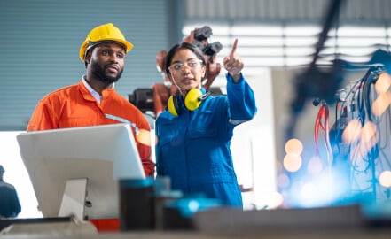 Man and woman in coveralls and safety gear pointing to array of wires