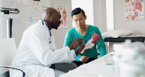 Doctor sitting at desk looking at model of body part with employee