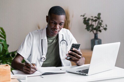 Man with lab coat and stethoscope taking notes in office