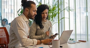 Man with laptop and woman with calculator at conference room table