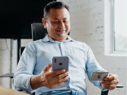 Relaxed man in office chair holding credit card and smartphone