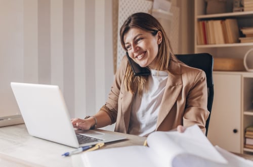 Smiling woman with laptop flipping through a report