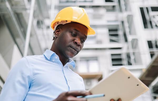 Man wearing a construction hard hat and looking at clipboard