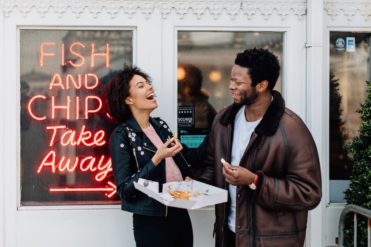 Man and woman standing outside Fish and Chips shop laughing and eating