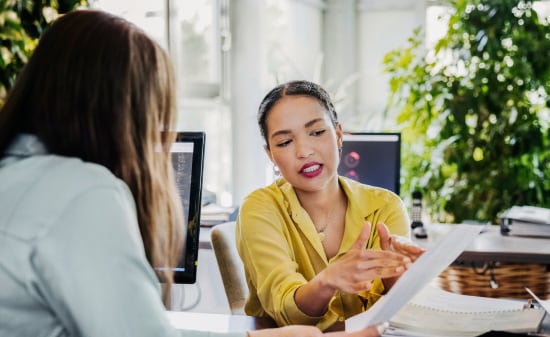 Two women in a private office conversing while going over a printout 