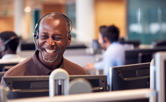 Smiling man at a busy call center having a phone call on a headset