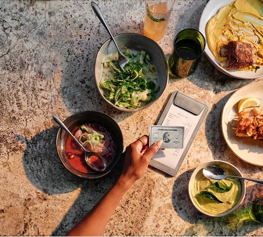 Person holding American Express Platinum® Card paying check at a table full of food