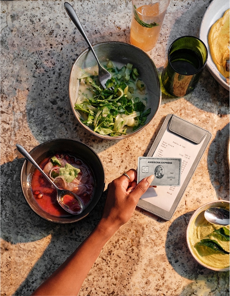 Person holding American Express Platinum® Card paying check at a table full of food
