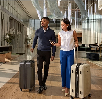 Two colleagues walking with luggage through a hotel lobby.