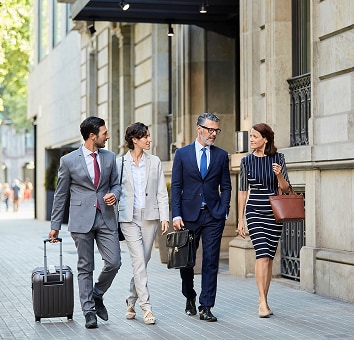 Man with suitcase walking on sidewalk with business colleagues.