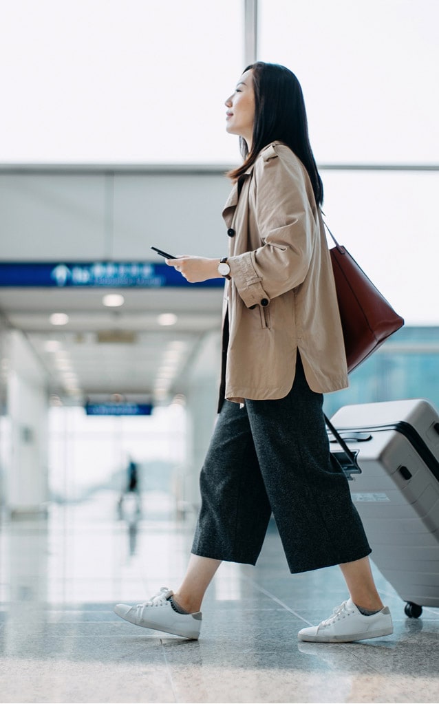 Woman with shoulder bag and suitcase, walking in airport.