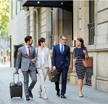 Four coworkers on a city street walking with their luggage.