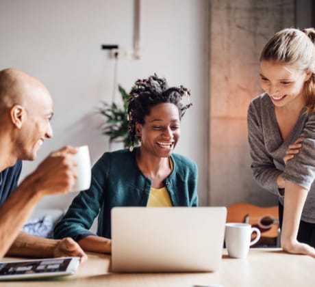 Three people smiling and looking at a laptop.