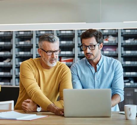 Two men sitting at a table, looking at the same open laptop