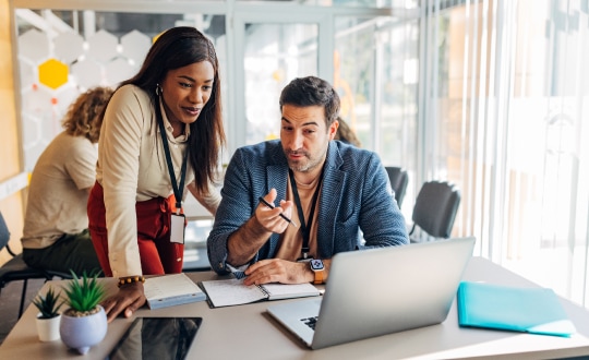 Two colleagues reviewing information on laptop at a desk.