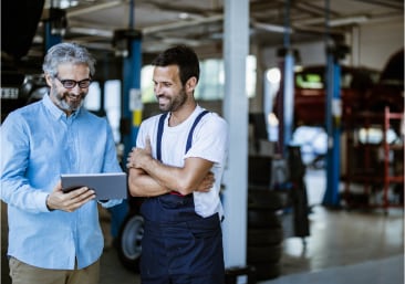 Two men reviewing information on tablet in a small auto shop.