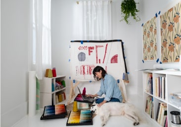 Woman working from home on a laptop, surrounded by art materials.