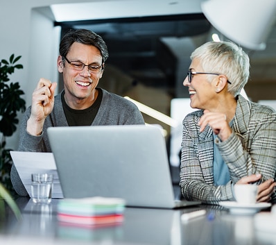 Two colleagues collaborating at a table with an open laptop.