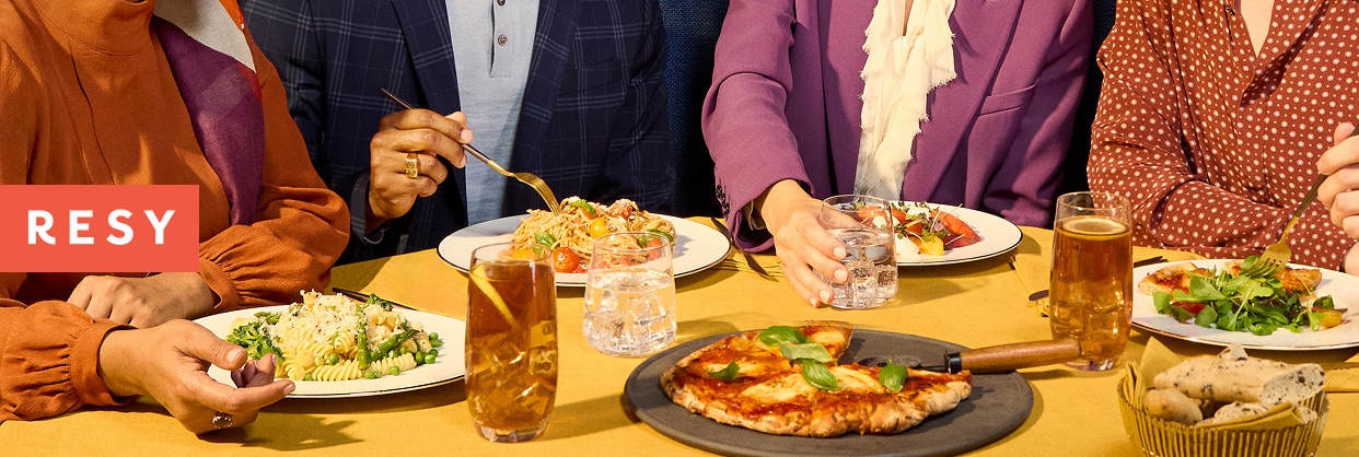 The Resy logo superimposed on a photo of a group dining at restaurant.