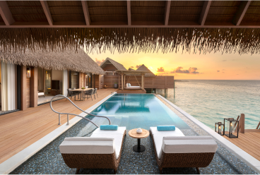 A serene pool and lounge area with a thatched roof, next to the ocean.