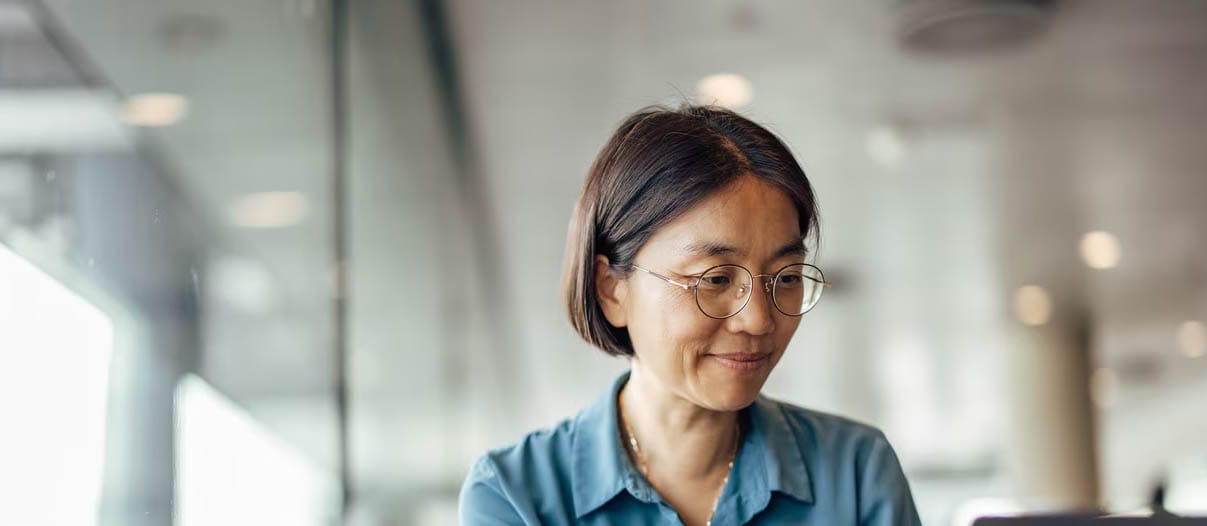 A woman wearing glasses is focused on her laptop, checking her credit score with a look of concentration.