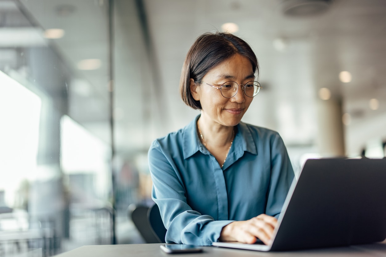 A woman wearing glasses is focused on her laptop, checking her credit score with a look of concentration.