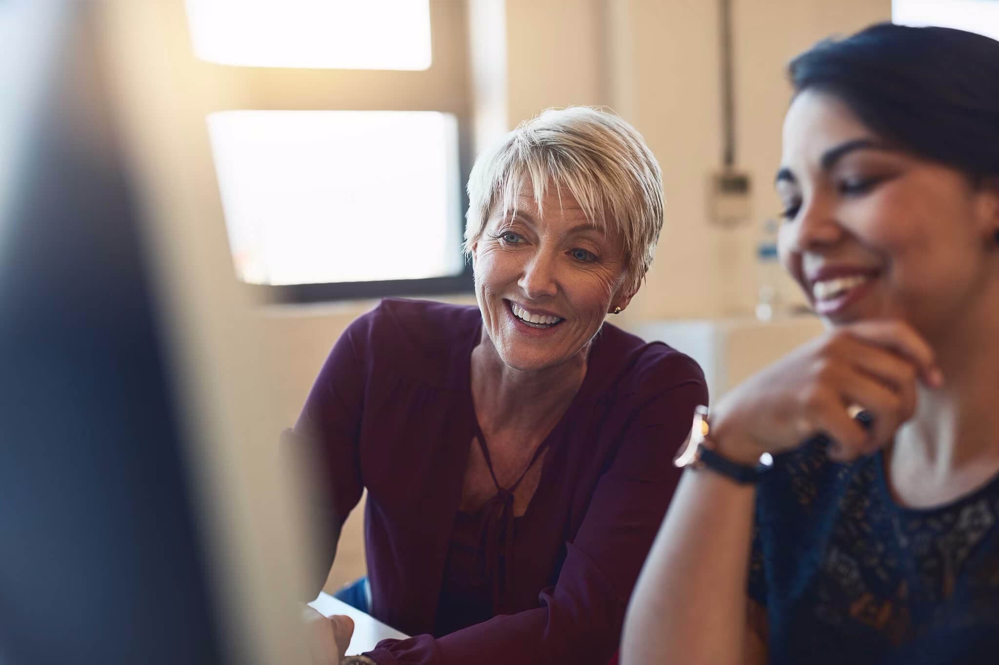 A woman smiles while seated beside another woman, symbolizing support in managing and protecting parents' finances.
