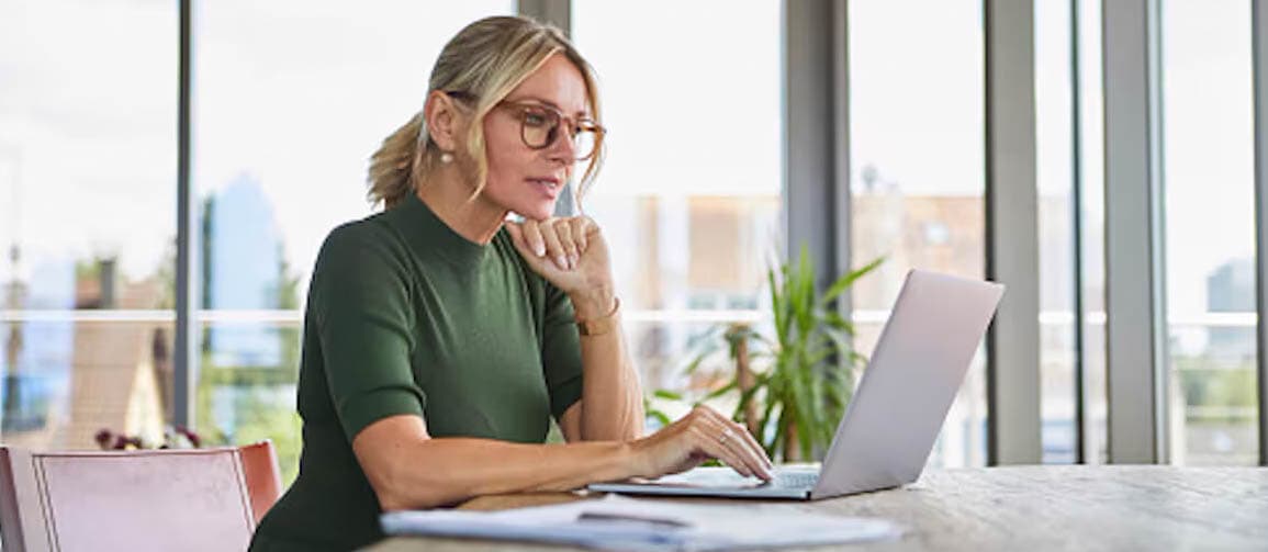 Woman is in the office with the city view, using the laptop