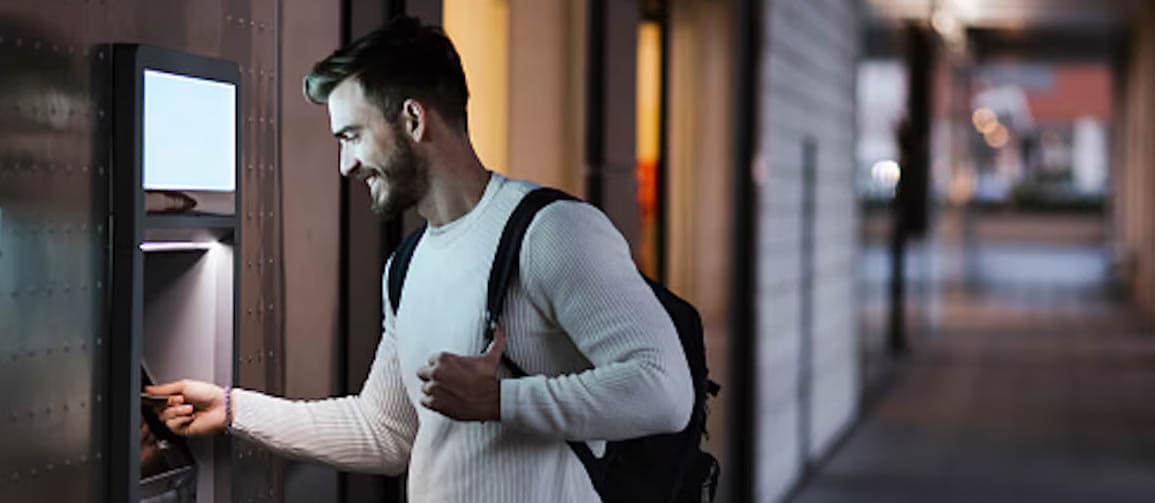 Man is using ATM outside in alley in evening time