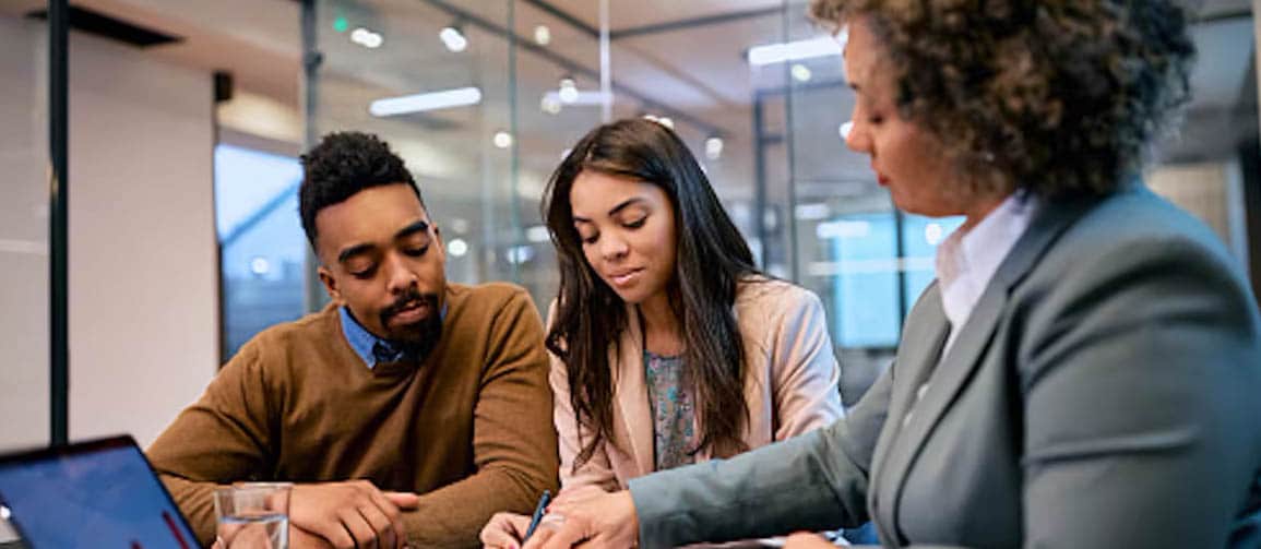 Man and two women are in the office, signing some paperwork at the table