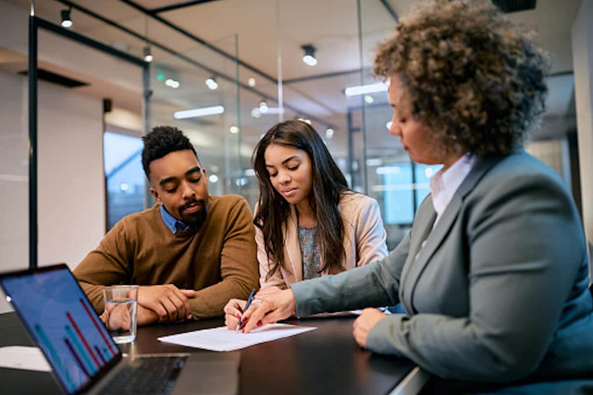 Man and two women are in the office, signing some paperwork at the table