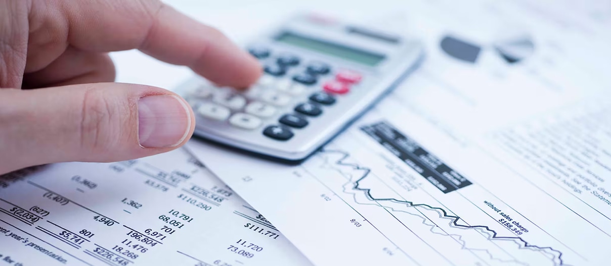 Close-up of a person's hand using a calculator on top of some paperwork
