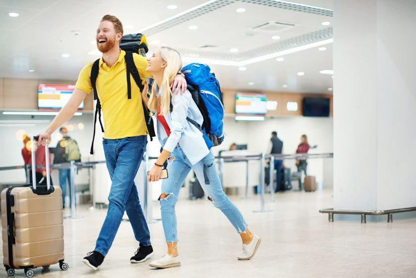 A man and woman carrying luggage navigate through an airport, ready for their journey and eager to earn travel points.