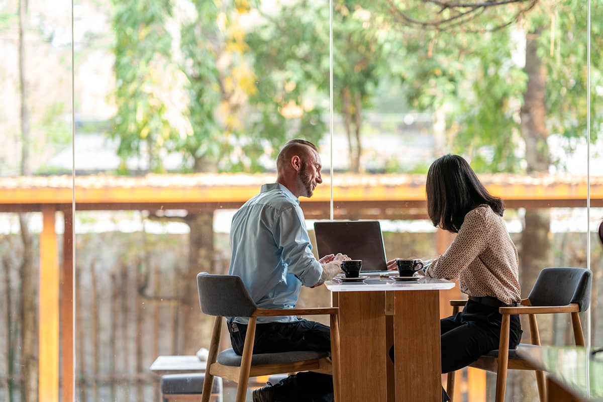A man and woman seated at a table, engaged with a laptop, discussing personal loan options together.