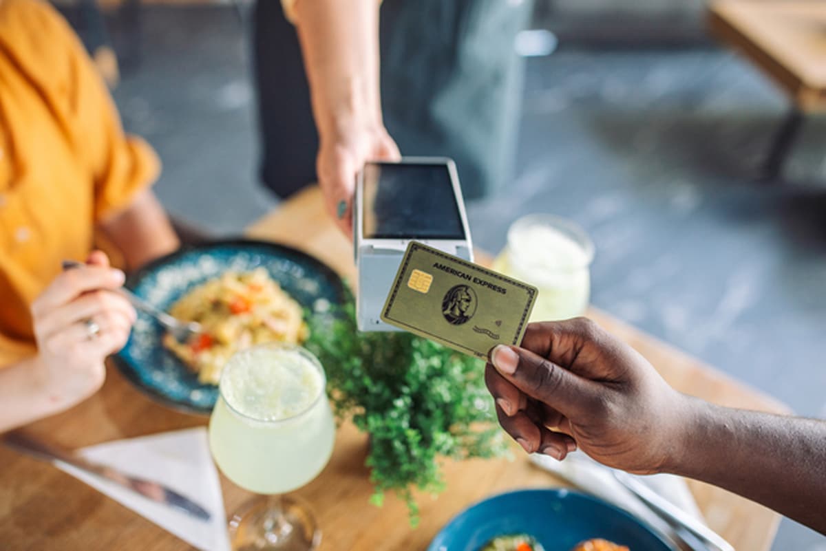 A person holding up their gold card to a handheld payment POS machine at a restaurant