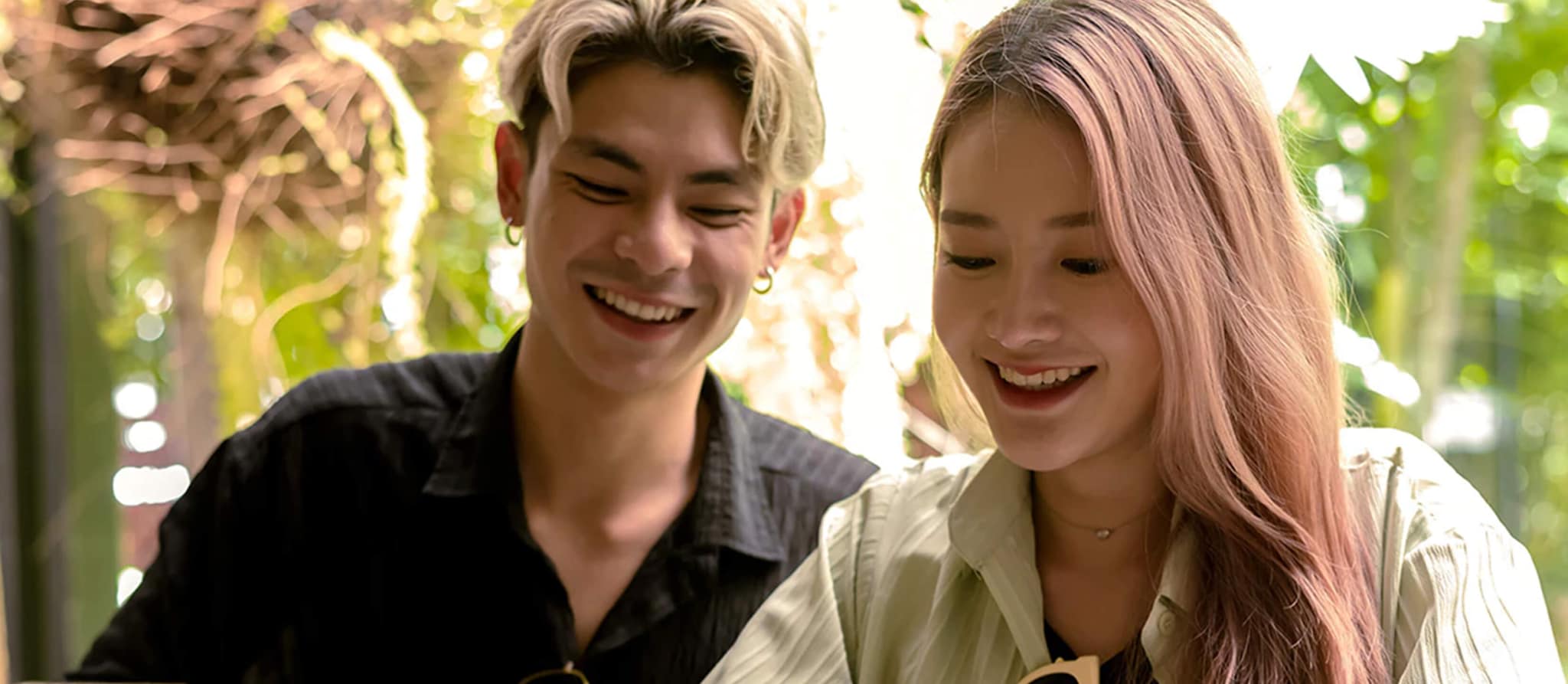 A young couple smiles at a table, engaging with a laptop, exploring options for American Express Hilton credit cards.