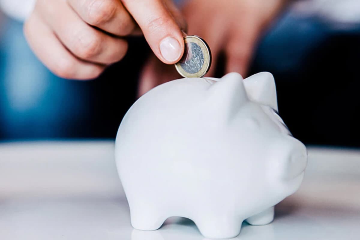  A person inserting a coin into a piggy bank, symbolizing savings and financial planning with an American Express® Savings Account.
