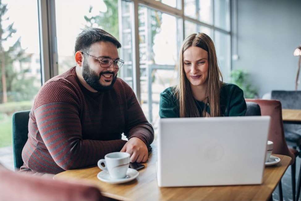 Two people sitting at a cafe looking at a laptop