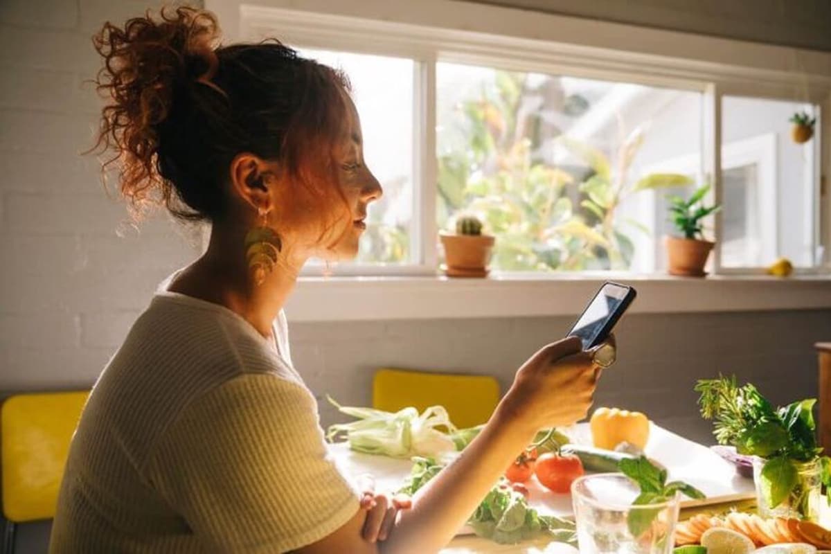 A woman, seated in front of a window, examines her phone, reflecting on the credibility of debt relief programs.