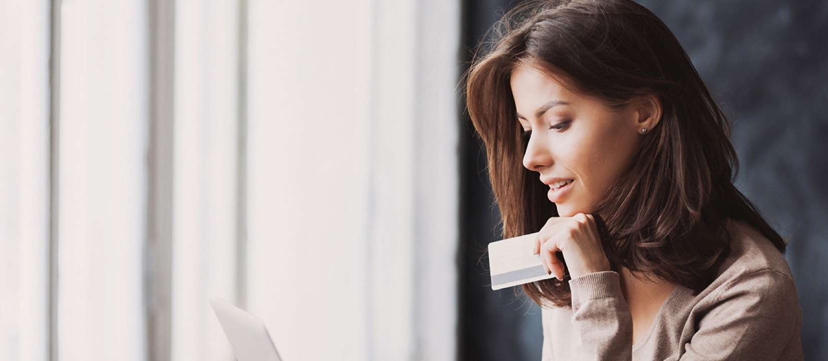 Woman is using a laptop and holding a credit card in coffee shop