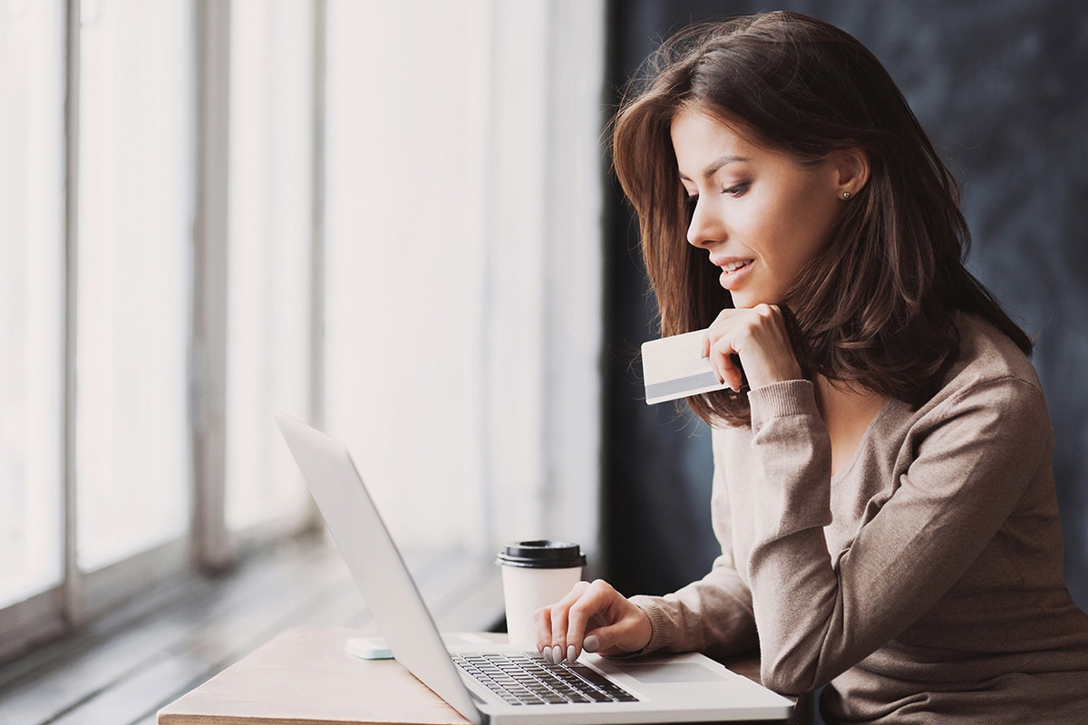 Woman is using a laptop and holding a credit card in coffee shop