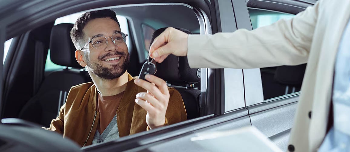A man sitting in the driver's seat of a car being handed the keys at the window