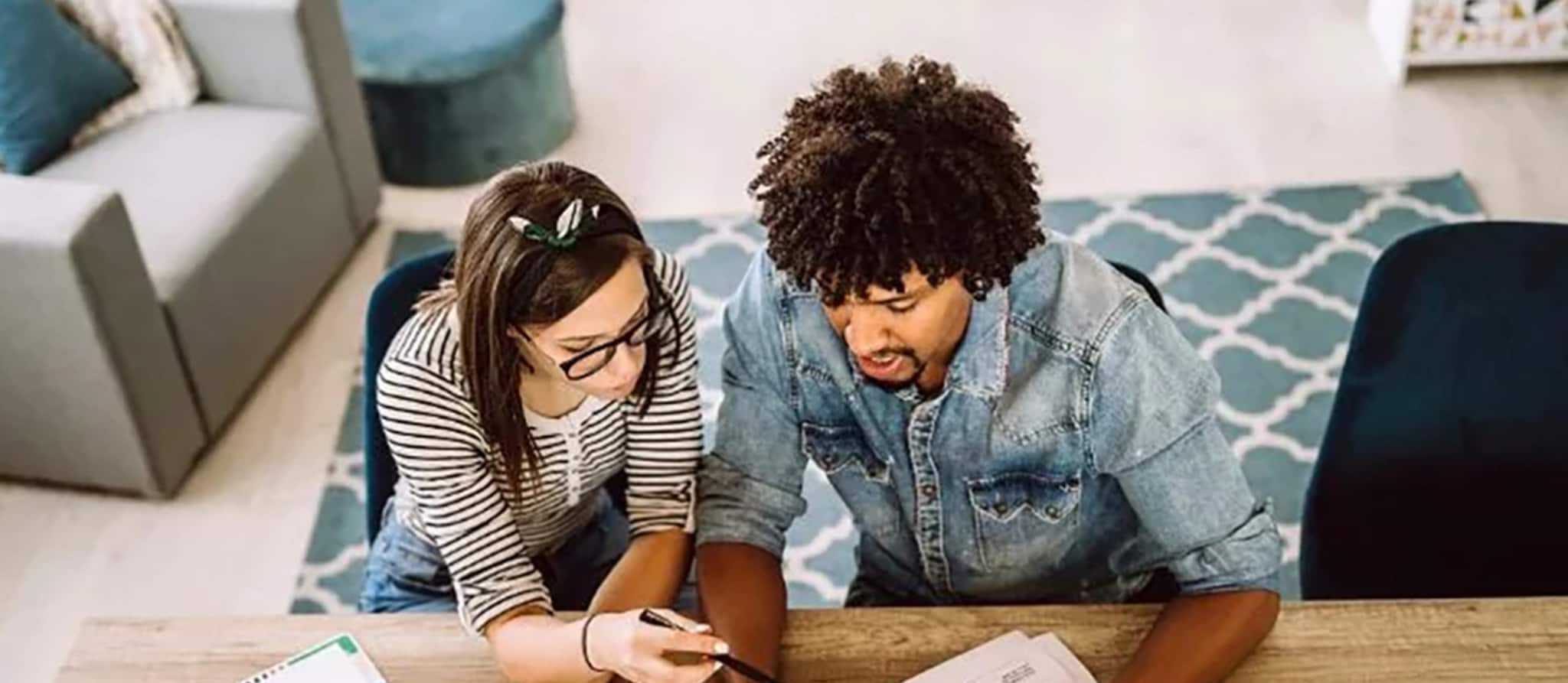 Two people at a table with laptops and papers, engaged in a conversation about handling credit card debt.