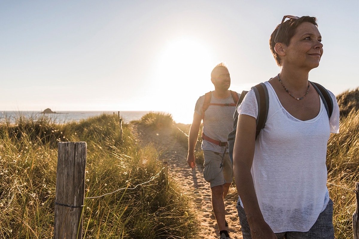 A man and woman enjoy a coastal walk, contemplating their journey and the advantages of a Roth Individual Retirement Account.